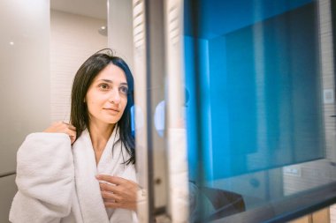 Beyaz cüppeli güzel beyaz kadın gülümsüyor ve aynada gururla kendine bakıyor.