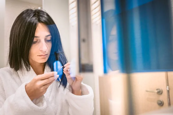 Pretty Woman in white robe suspiciously touching her hair ends in bathroom