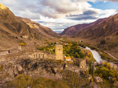 Khetvisi kalesi havadan bakıldığında renkli sonbahar doğasıyla çevrili ve arka planda paravani nehri ve dramatik gökyüzü var. Gürcistan 'ın tarihi manzaraları.