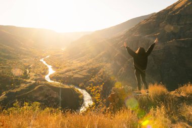 Siyahlı kadın kayalık yüzeyde elleri açık bir şekilde dramatik bir altın sonbahar manzarasının önünde duruyor. Gürcistan, Kafkasya 'da seyahat.