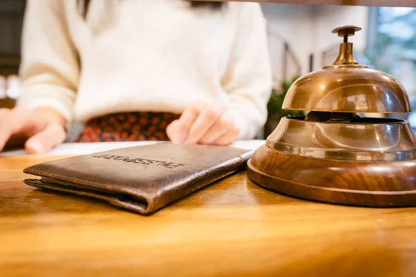 Giant hotel bell ring standing on wooden check in tablewith person standing and handing passport. Travel and stays in hotels.2020