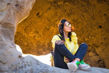 Genç dişi Gürcü bacak bacak üstüne atarak oturur ve bir kayanın içine bakar.