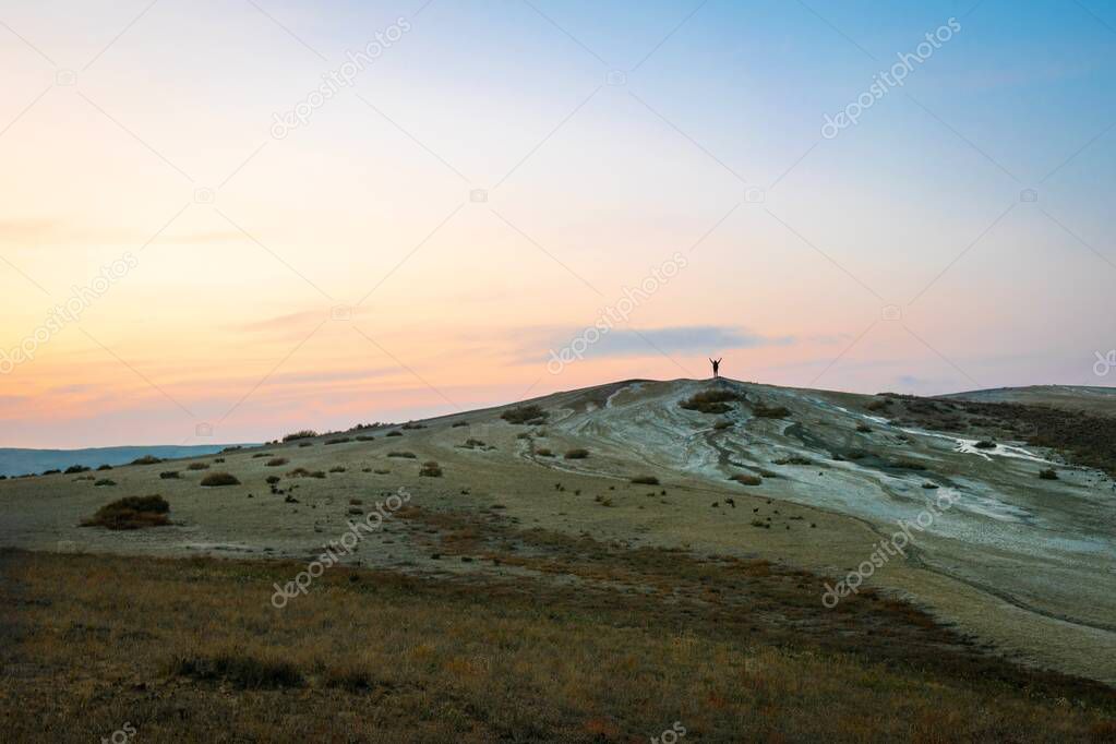 Female person sillhouette standing on mud volcanoe with spreaded hands. Travel and exploration in caucasus.