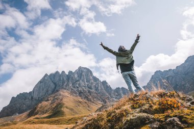 Elleri keyiften havada kayanın üstünde duran kadının alçak açısı arka plandaki yüksek dağa bakıyor. Tek kişilik macera ve seyahat konsepti