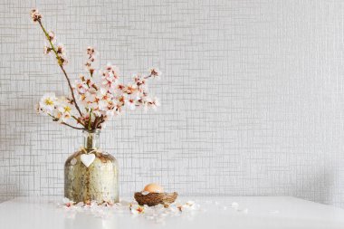 Vazoda taze beyaz papatyalar, beyaz masada paskalya yumurtası süslemeleri ve gri duvar kağıdı arka planlı vazolar.