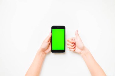 Kadının elinde yeşil ekranlı cep telefonu var. Yeşil arka planda izole edilmiş ve başparmakları havada. Mobil ekran boşluğunu düzenle