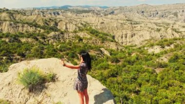 Güzel kadın turist, yaz tatilinde güneşli bir gün ışığında manzaralı bir yerde selfie çekiyor. Hava sinematografisi seyahat macera konsepti