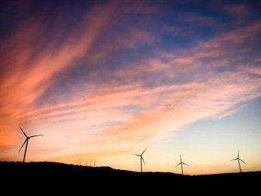 Gökyüzü arkaplan manzaralı yeşil alanda duran beş rüzgar türbini. Yenilenebilir enerji konseptini kopyala