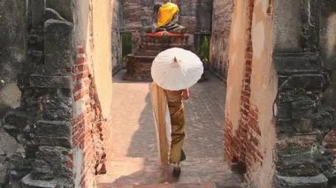 Tayland, Ayutthaya - 15 Mart 2023: Geleneksel Tayland elbiseli kadın şemsiye gezisi tarihi Buda heykelini ziyaret etti. Kavram mirası, maneviyat, thai kültürü