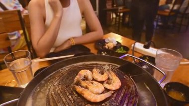 Bangkok restoranında karides pişiren bir kadın Bangkok restoranında ızgara karides pişiriyor. Çorba ve barbekü pişirme tarzını deniz ürünleri, yemek çubukları ve soslarla birleştiriyor.