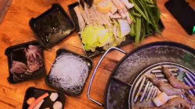 Geleneksel Tayland BBBQ bifteği (Moo Krata), karışık deniz ürünleri, ahtapot, karides, balık köftesi, erişte, mantar, lahana, mısır, sarımsak ve Tayland, Bangkok 'ta ahşap masaya soslar..