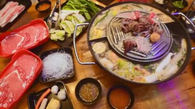 Geleneksel Tayland BBBQ bifteği (Moo Krata), karışık deniz ürünleri, ahtapot, karides, balık köftesi, erişte, mantar, lahana, mısır, sarımsak ve Tayland, Bangkok 'ta ahşap masaya soslar..