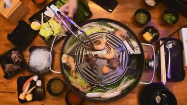 Geleneksel Tayland BBBQ bifteği (Moo Krata), karışık deniz ürünleri, ahtapot, karides, balık köftesi, erişte, mantar, lahana, mısır, sarımsak ve Tayland, Bangkok 'ta ahşap masaya soslar..