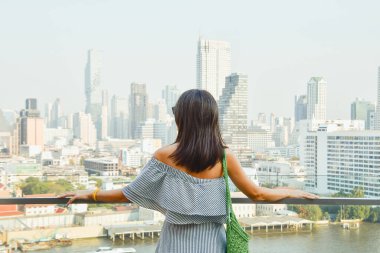 Genç ve güzel bir kadın Bangkok şehrinin gökyüzü manzarasının tadını çıkarıyor. Şehir gözlem rıhtımında ünlü bir alışveriş merkezi. Bağımsız iş kadını. Arka plan parlak filtresi
