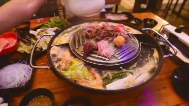 Geleneksel Tayland BBBQ bifteği (Moo Krata), karışık deniz ürünleri, ahtapot, karides, balık köftesi, erişte, mantar, lahana, mısır, sarımsak ve Tayland, Bangkok 'ta ahşap masaya soslar..