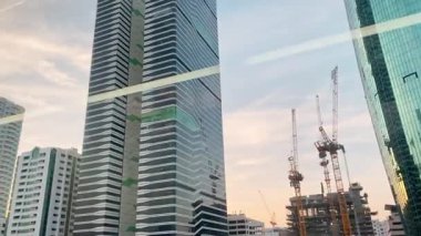 Dubai, BAE - 24 Ocak 2026: Dubai ufuk çizgisi günbatımında metro penceresinden modern yerleşim kuleleri kentsel büyüme ulaşım altyapısı emlak yatırım kavramını gösteriyor