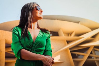 Doha, Katar - 25 Ocak 2026: Çağdaş Ortadoğu kültür lüks kentsel yaşam tarzını temsil eden ikonik çöl gülü mimarisi ile Ulusal Müze Katarı 'nın yanında duran kadın