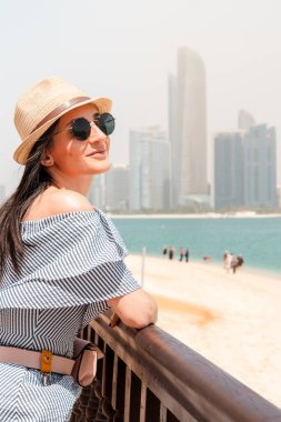 Ebu Dabi siluetinin çarpıcı zeminine karşı çekici bir kadın turist, kendine güvenen genç bir kadın renkli bir türban takıyor, BAE 'yi tanımlayan çeşitlilik ve ayrıcalık ruhunu somutlaştırıyor.