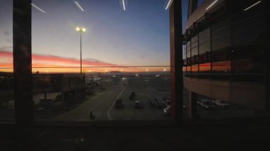 İstanbul, Türkiye - 10 Aralık 2025: Gün doğumunda park halindeki hava araçlarının yer destek araçları pist aydınlatması ve yansıtıcı cam cephe ile apron üzerindeki zaman aşımına uğramış havaalanı terminali penceresi görüntüsü