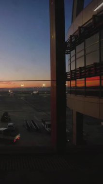 İstanbul, Türkiye - 10 Aralık 2025: Gün doğumunda park halindeki hava araçlarının yer destek araçları pist aydınlatması ve yansıtıcı cam cephe ile apron üzerindeki zaman aşımına uğramış havaalanı terminali penceresi görüntüsü