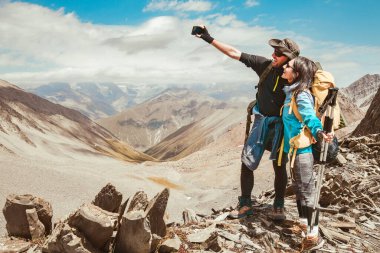 Dağın tepesinde fotoğraf çeken mutlu yürüyüşçüler, kameraya gülümseyen sırt çantalı iki gezgin, gezgin blogcu...