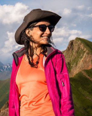 Georgia 'nın Kazbegi Ulusal Parkı dağlarında gülümseyen şapkalı ve ceketli Mutlu Genç Gezgin kadın portresi macera yaşam tarzı ve yürüyüş portresi