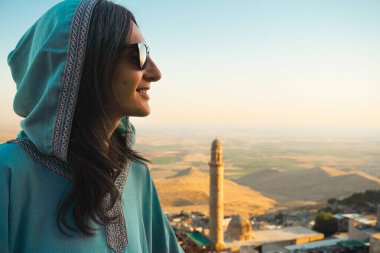 Günbatımında Mezopotamya düzlükleri ve tarihi cami minaresi panoramik manzarasıyla Mardin 'in üzerinde duran abaya' da gülümseyen kadın gezgin