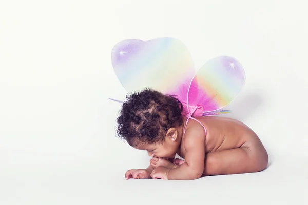 Lovely baby girl tasting her foot while wearing wings — Stock Photo, Image