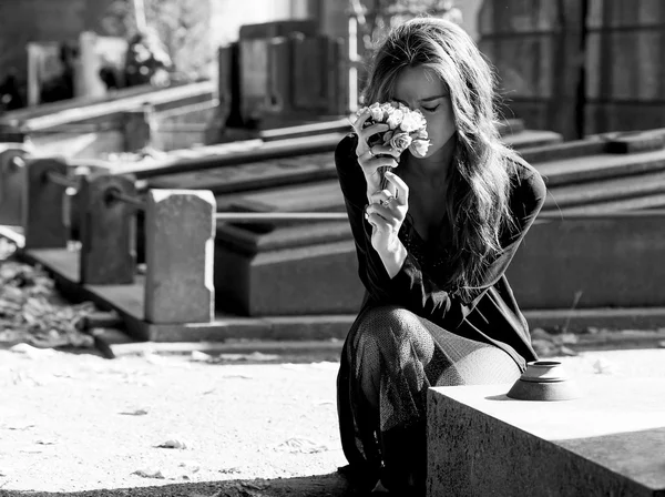 Mulher triste segurando um monte de flores perto de uma sepultura monocromática — Fotografia de Stock