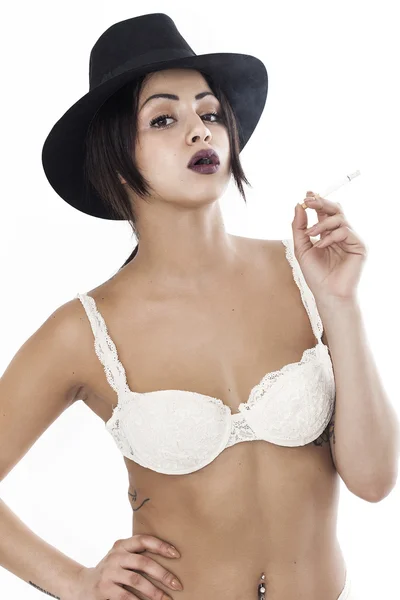 Woman wearing white lingerie and black hat while smoking cigaret — Stock Photo, Image