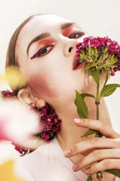 Vacker flicka stående att lukta blommor och tittar på kameran — Stockfoto