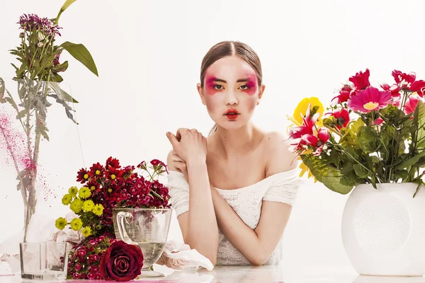 Vacker flicka sitter vid bordet med blommor — Stockfoto