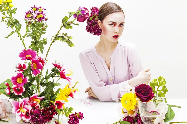 Schöne Frau sitzt am Tisch mit Blumen — Stockfoto