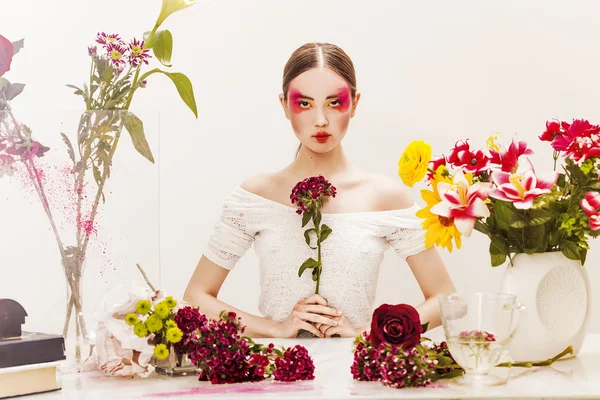 Mädchen Schönheit Porträt sitzt am Tisch mit bunten Blumen — Stockfoto