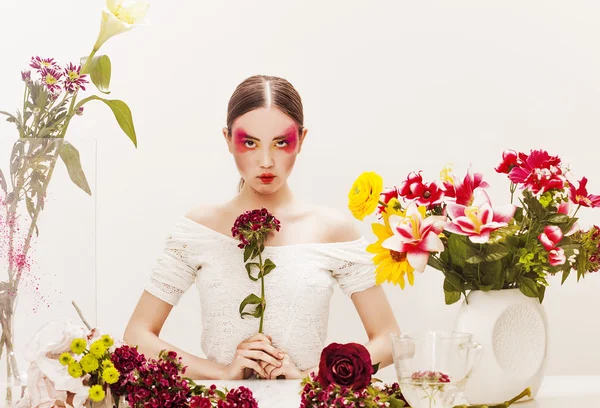 Meisje schoonheid portret zit aan de tafel met kleurrijke bloemen — Stockfoto