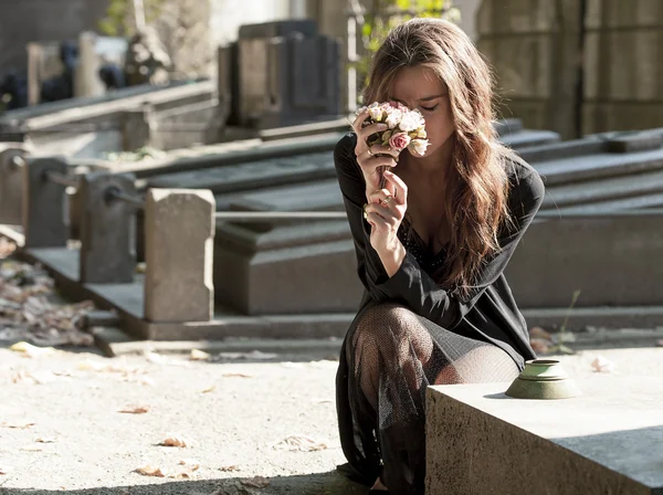 Sad woman holding bunch of flowers near a grave — Stock Photo, Image