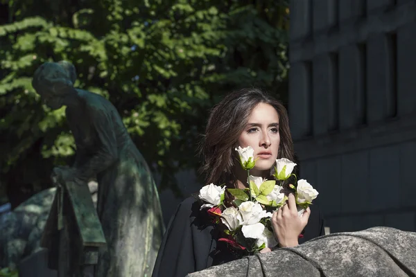 Sorgliga kvinna stående anläggning vita rosor nära en grav — Stockfoto