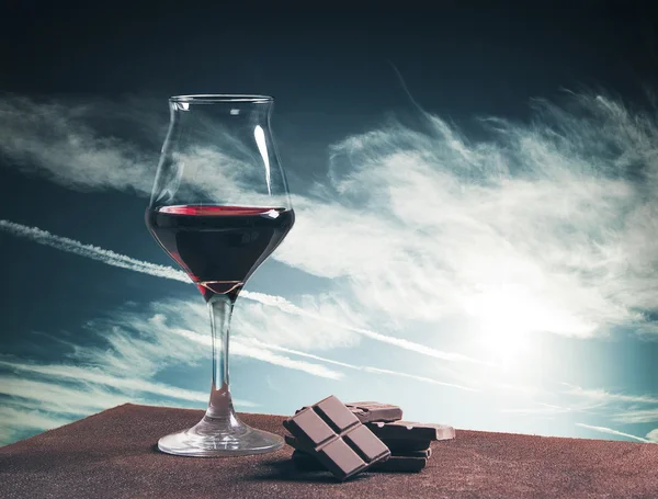 Bicchiere di vino e cioccolato con paesaggio nuvoloso blu — Foto Stock