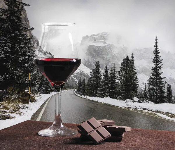 Copa de vino tinto y chocolate con carretera de montaña de invierno — Foto de Stock
