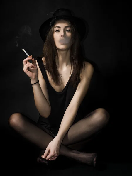 Hermosa chica retrato sentado y usando sombrero mientras fuma ci —  Fotos de Stock