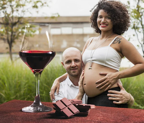 Red wine glass and chocolate with pretty couple expecting baby — Stock Photo, Image