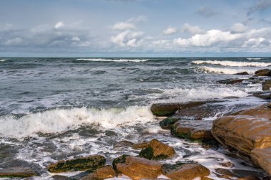 Boş kayalık plaj ve bulutlu havada fırtınalı deniz