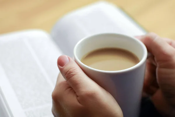 Cup of coffee in hands, reading bible