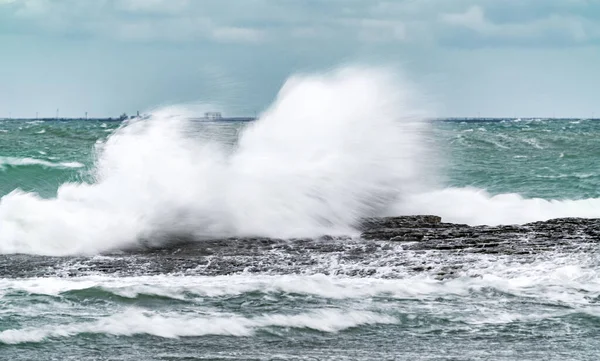 A huge wave crashes on a rocky shore