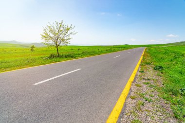 Asfalt yolu mavi gökyüzü ve bulutlar arasında yeşil tarım alanları arasında