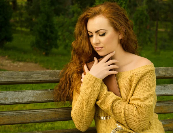 Ingefära-haired kvinna sitter på en bänk med bok — Stockfoto