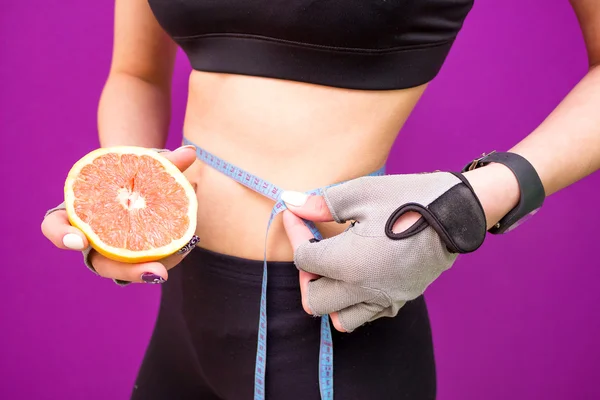 Стройная молодая женщина измеряет свою тонкую талию рулеткой и грейпфрутом — стоковое фото