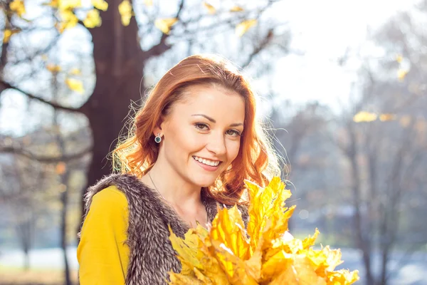 Glücklich lächelnde junge Frau mit einem Bund gelb gefärbtem Ahornblatt — Stockfoto