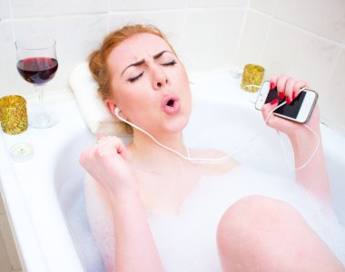 Young woman  listening music while lying in the bath with foam and candles