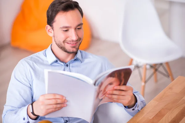 Agradable hombre sonriente leyendo una revista — Foto de Stock